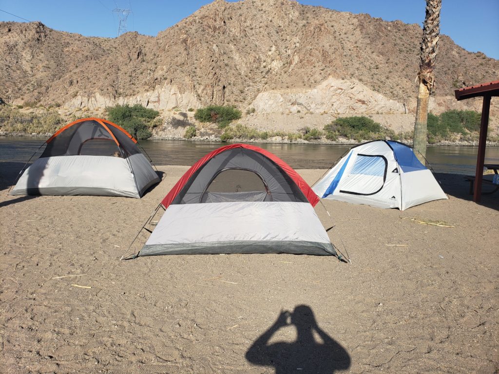 Three tents at a campsite by a river